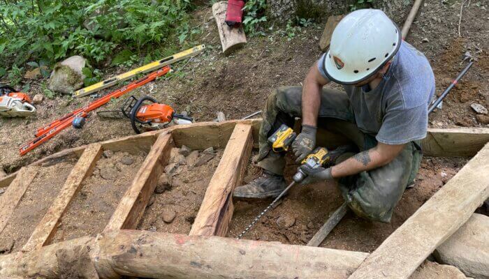 Crew member uses a drill to secure steps of locust log staircase on Bullhead Trail