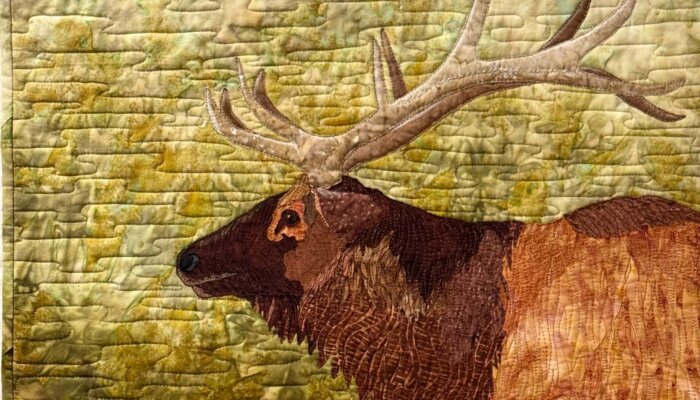 Quilt with an elk design created by fabric and stitches.
