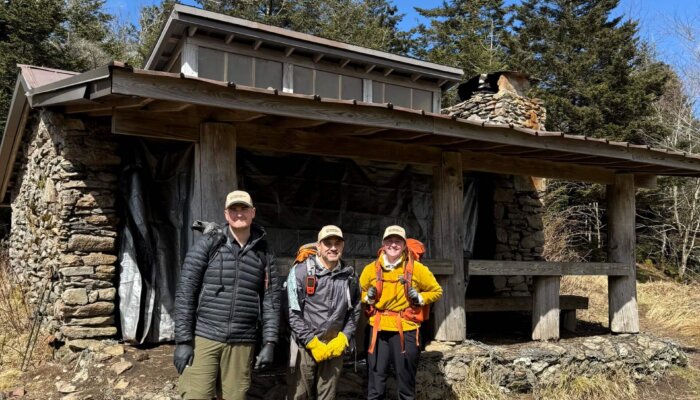 Three Ridgerunners stand beside the Icewater Spring Shelter