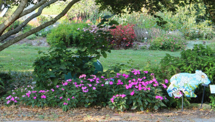 Painted wood bear displayed in a garden with pink flowers, bushes and a metal bench